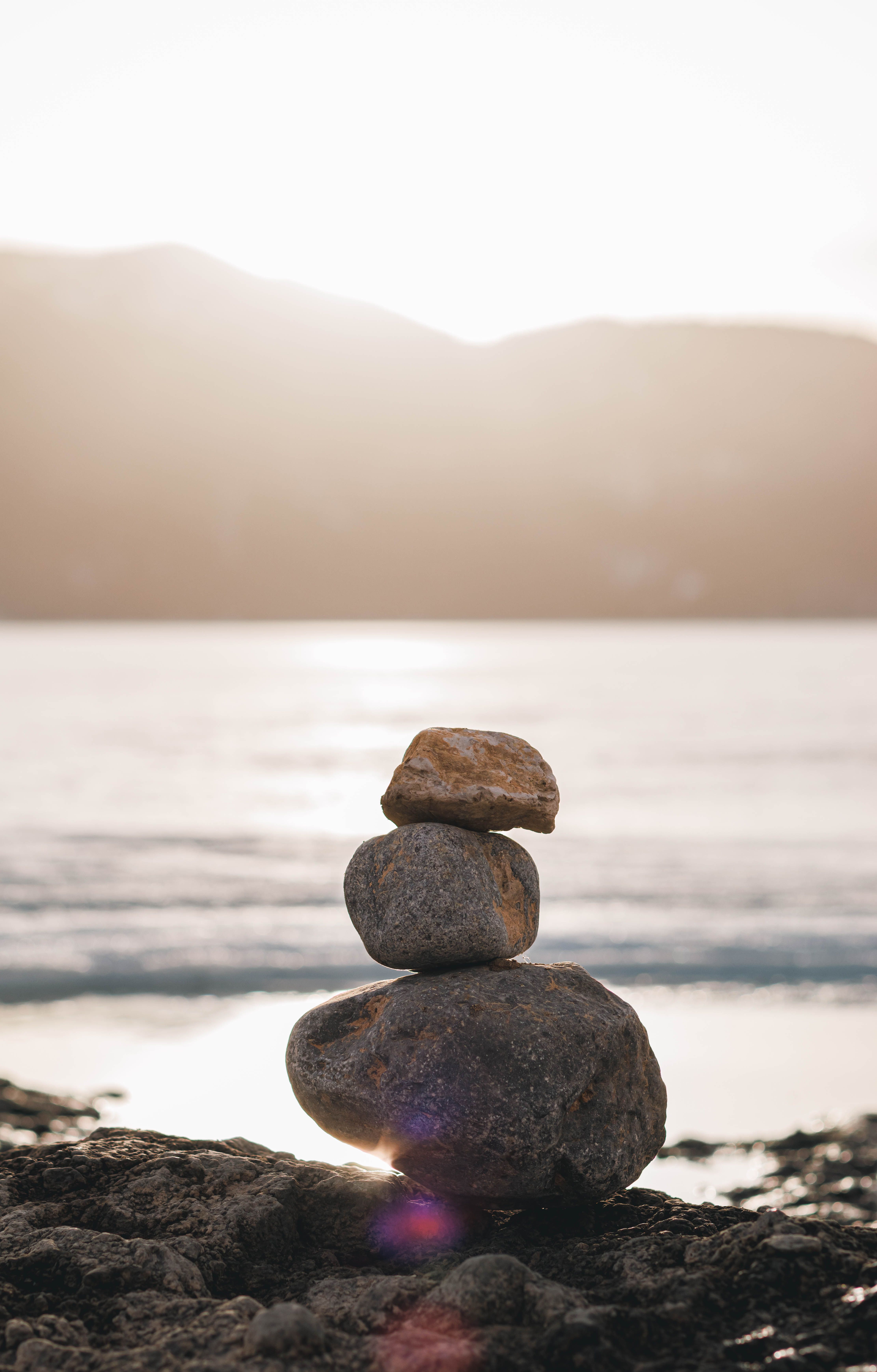 Balanced stones on a quiet shoreline at sunrise, mist rising over still water